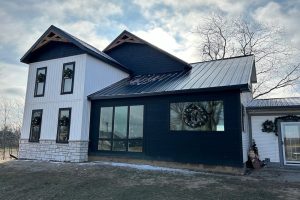 Modern farmhouse with white board-and-batten, black siding, black metal roof, white limestone, and black-trimmed windows.