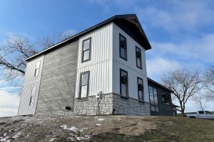 Modern farmhouse with white board-and-batten, black siding, black metal roof, white limestone, and black-trimmed windows.