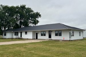 Black standing seam metal roof on a white ranch house