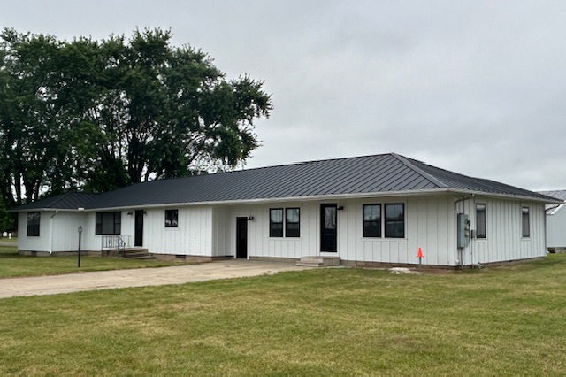 Black standing seam metal roof on a white ranch house